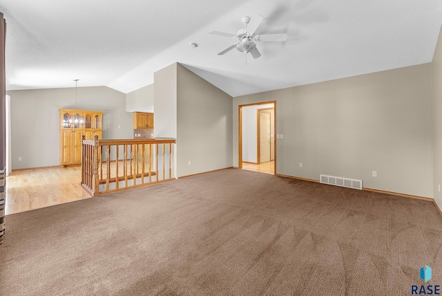 carpeted spare room featuring ceiling fan with notable chandelier and lofted ceiling