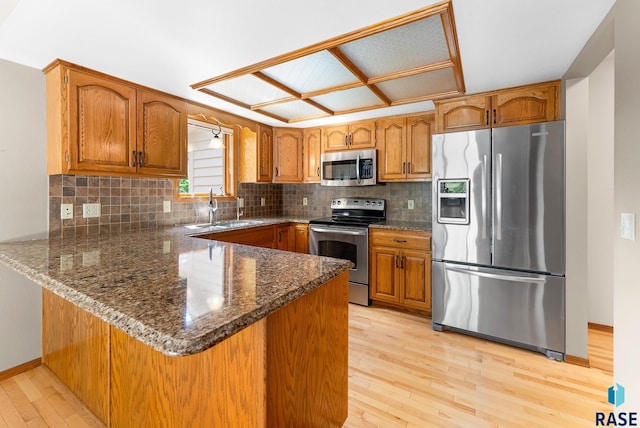 kitchen with sink, dark stone countertops, light hardwood / wood-style floors, kitchen peninsula, and stainless steel appliances