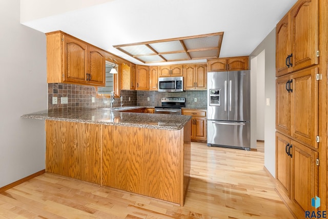 kitchen with light wood-type flooring, kitchen peninsula, stainless steel appliances, and tasteful backsplash