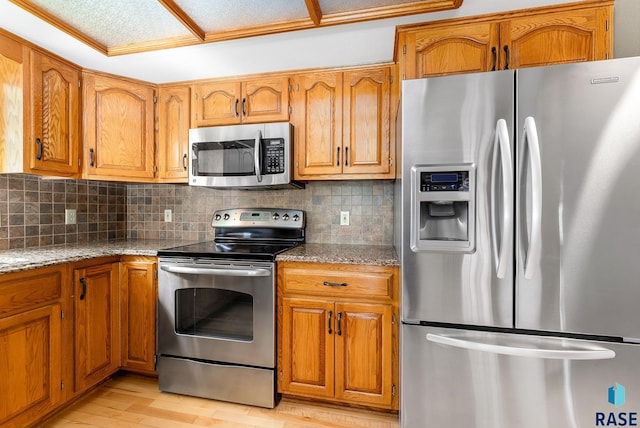 kitchen featuring decorative backsplash, light hardwood / wood-style flooring, light stone countertops, and appliances with stainless steel finishes