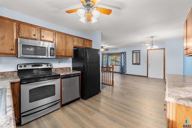 kitchen featuring ceiling fan with notable chandelier, stainless steel appliances, and light hardwood / wood-style flooring