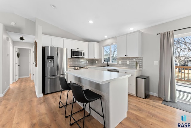 kitchen featuring appliances with stainless steel finishes, a kitchen breakfast bar, white cabinets, a kitchen island, and lofted ceiling