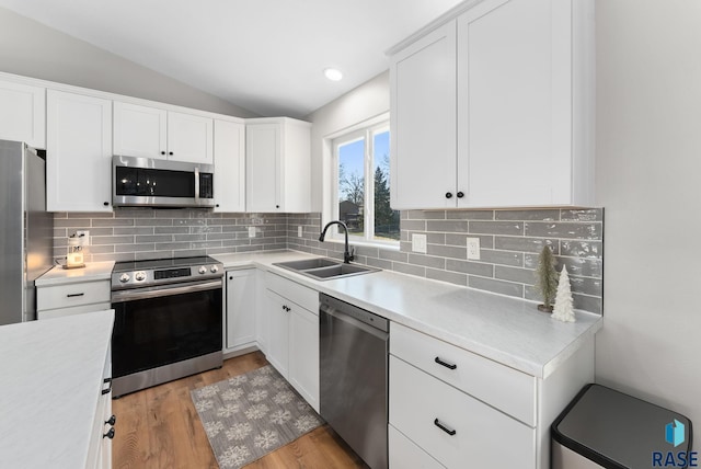 kitchen with appliances with stainless steel finishes, light wood-type flooring, vaulted ceiling, sink, and white cabinets