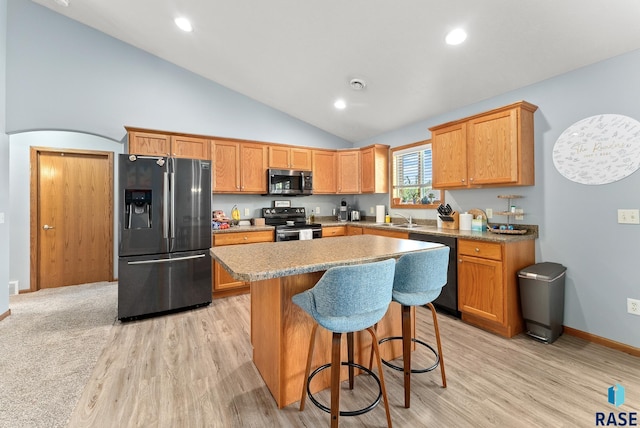 kitchen featuring appliances with stainless steel finishes, light wood-type flooring, sink, a kitchen island, and a breakfast bar area