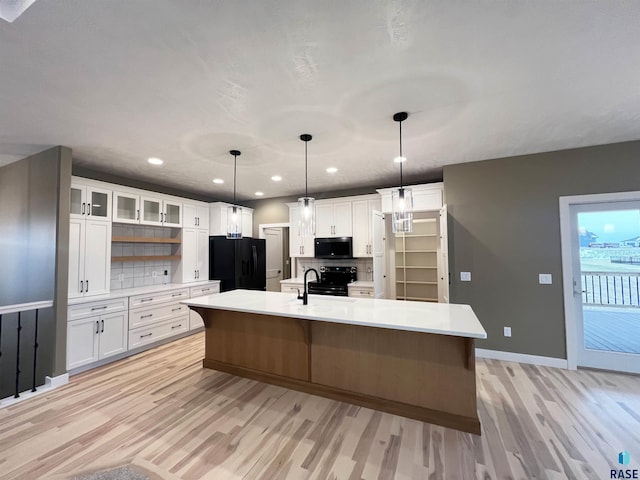 kitchen with white cabinetry, hanging light fixtures, tasteful backsplash, black appliances, and a center island with sink