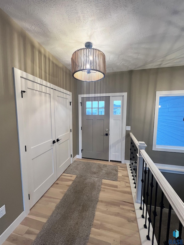 entryway with light hardwood / wood-style flooring, a chandelier, and a textured ceiling