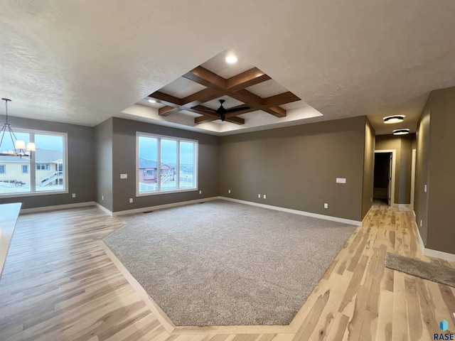 unfurnished living room with beamed ceiling, a healthy amount of sunlight, coffered ceiling, and light wood-type flooring