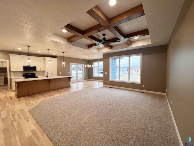 unfurnished living room featuring ceiling fan with notable chandelier, sink, coffered ceiling, beam ceiling, and light hardwood / wood-style flooring