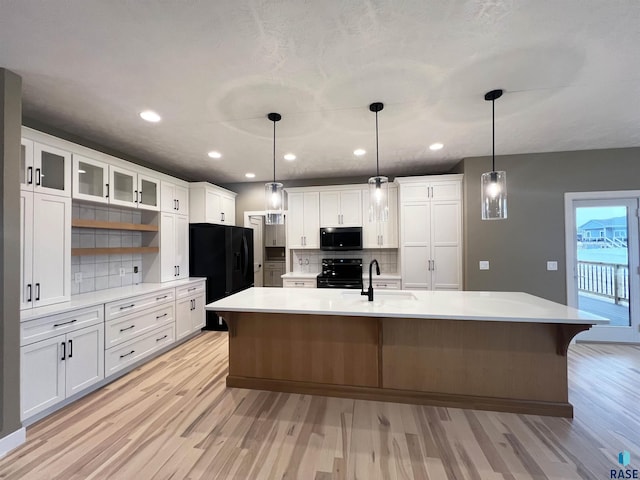 kitchen featuring white cabinetry, an island with sink, and black appliances