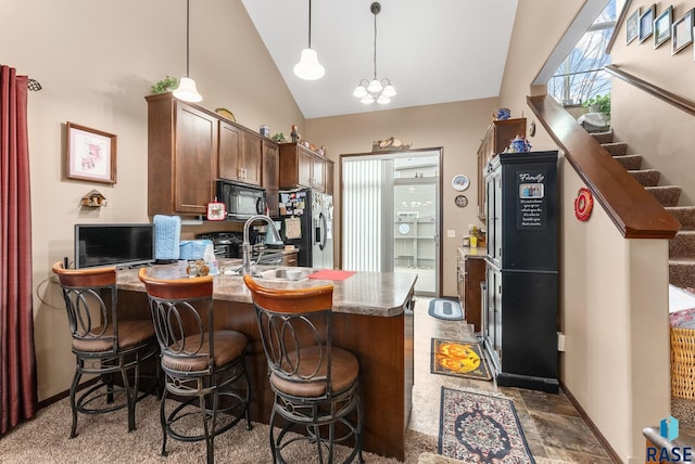 kitchen with a kitchen bar, stainless steel refrigerator with ice dispenser, high vaulted ceiling, an inviting chandelier, and hanging light fixtures