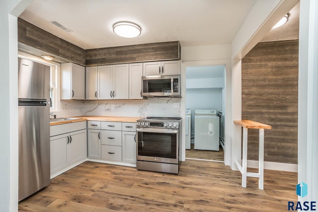 kitchen featuring butcher block counters, stainless steel appliances, separate washer and dryer, white cabinets, and hardwood / wood-style flooring