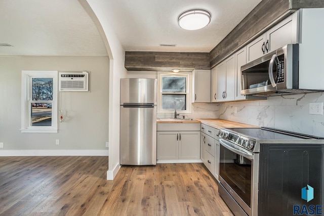 kitchen with white cabinetry, sink, light hardwood / wood-style flooring, an AC wall unit, and appliances with stainless steel finishes