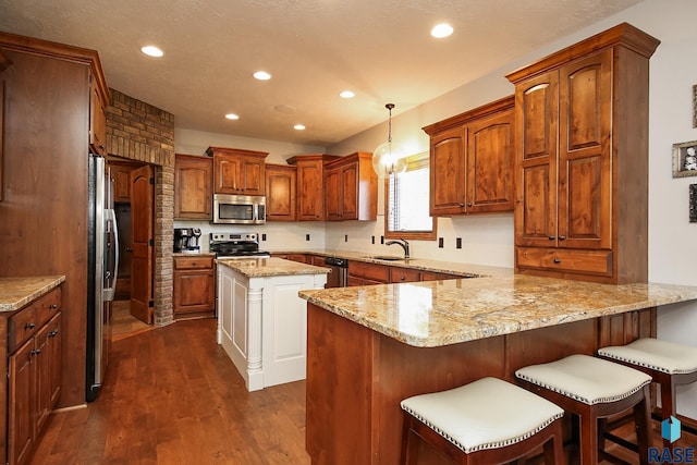 kitchen featuring appliances with stainless steel finishes, hanging light fixtures, kitchen peninsula, dark wood-type flooring, and sink