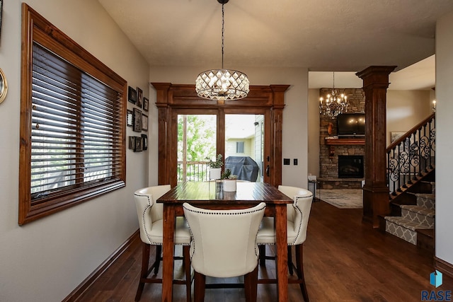 dining room with a fireplace, an inviting chandelier, dark hardwood / wood-style flooring, and ornate columns