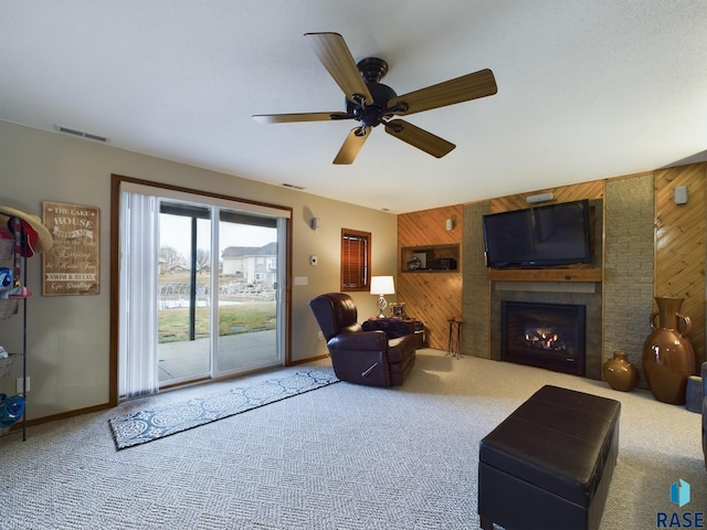 carpeted living room featuring wood walls, a large fireplace, and ceiling fan