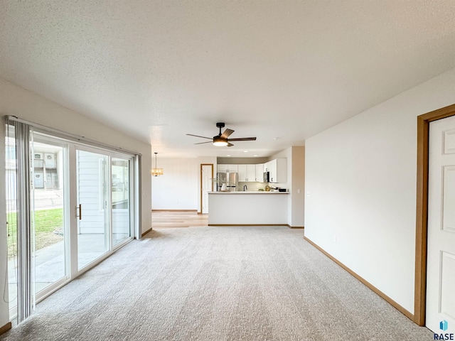 unfurnished living room with light carpet, ceiling fan, and a textured ceiling