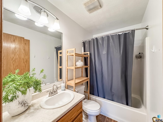 full bathroom featuring shower / tub combo with curtain, vanity, a textured ceiling, and toilet