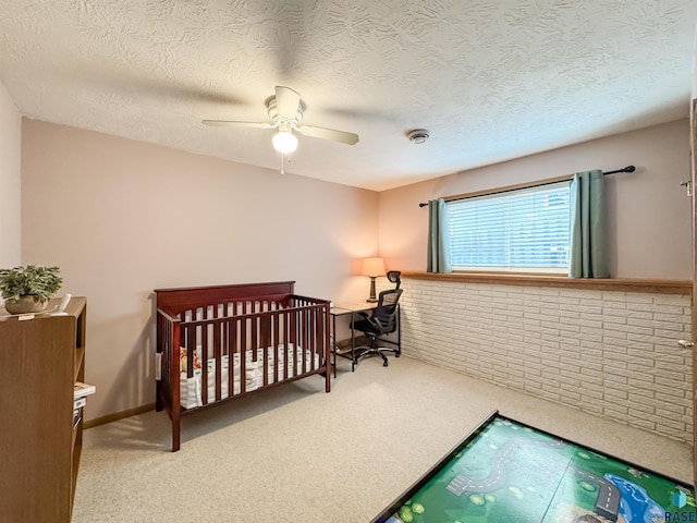 carpeted bedroom featuring a textured ceiling, a nursery area, and ceiling fan