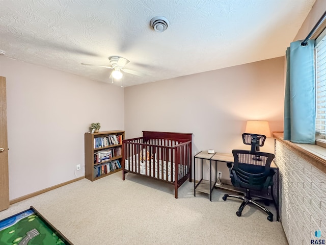 carpeted bedroom with ceiling fan, a textured ceiling, and a nursery area