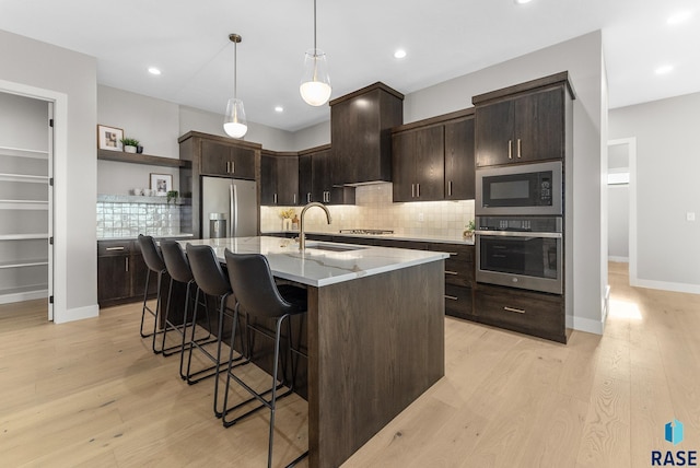 kitchen featuring light stone counters, custom exhaust hood, stainless steel appliances, sink, and an island with sink