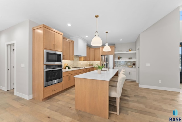 kitchen with a breakfast bar, hanging light fixtures, light hardwood / wood-style flooring, an island with sink, and appliances with stainless steel finishes