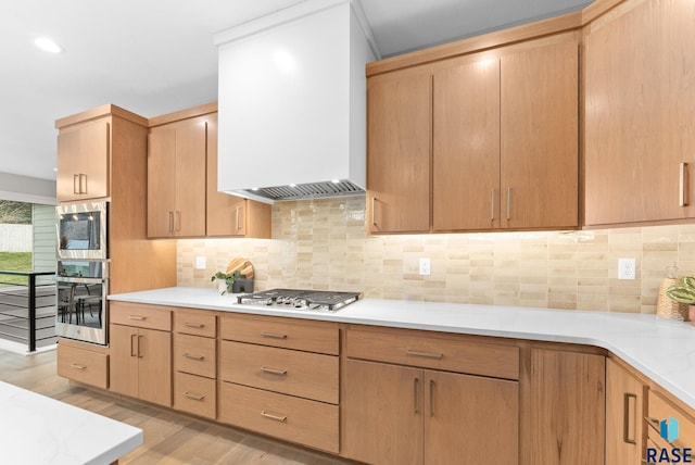 kitchen with custom exhaust hood, light brown cabinets, decorative backsplash, light hardwood / wood-style floors, and stainless steel appliances