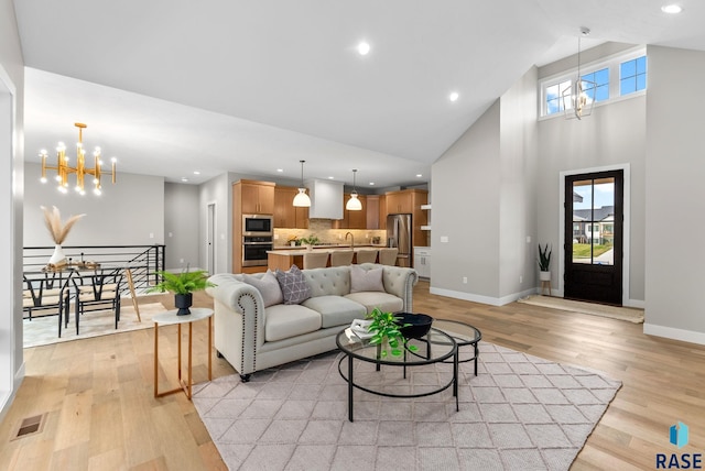 living room featuring sink, high vaulted ceiling, a chandelier, and light wood-type flooring