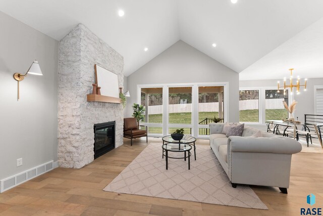 living room featuring high vaulted ceiling, light hardwood / wood-style flooring, a stone fireplace, and a notable chandelier