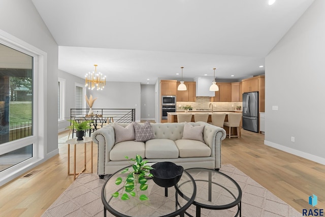 living room featuring vaulted ceiling, sink, a notable chandelier, and light wood-type flooring