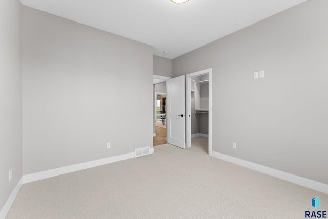 unfurnished bedroom with a walk in closet, light colored carpet, and a closet