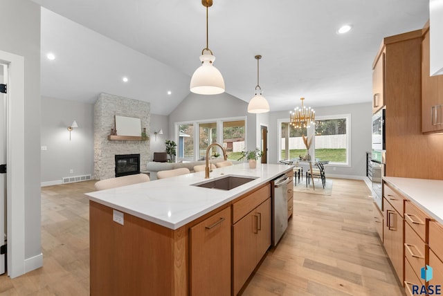 kitchen featuring sink, pendant lighting, a center island with sink, dishwasher, and a stone fireplace