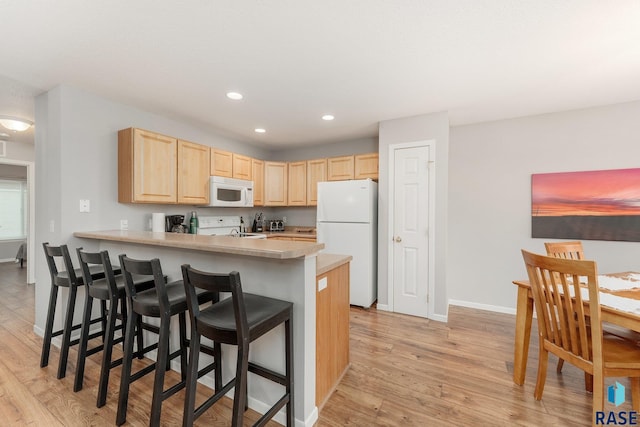 kitchen with kitchen peninsula, white appliances, light brown cabinetry, a breakfast bar, and light wood-type flooring