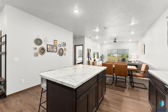 kitchen featuring ceiling fan, dark hardwood / wood-style flooring, a kitchen island, a kitchen bar, and dark brown cabinets