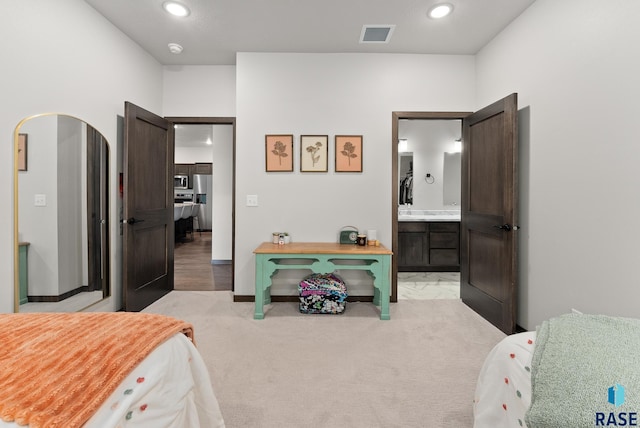 bedroom with stainless steel fridge, light colored carpet, and connected bathroom