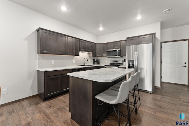 kitchen featuring dark brown cabinetry, sink, stainless steel appliances, dark wood-type flooring, and a kitchen island