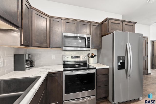 kitchen with tasteful backsplash, light stone counters, dark brown cabinets, and stainless steel appliances