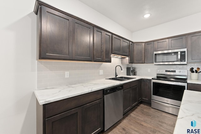 kitchen with dark brown cabinetry, sink, stainless steel appliances, tasteful backsplash, and wood-type flooring