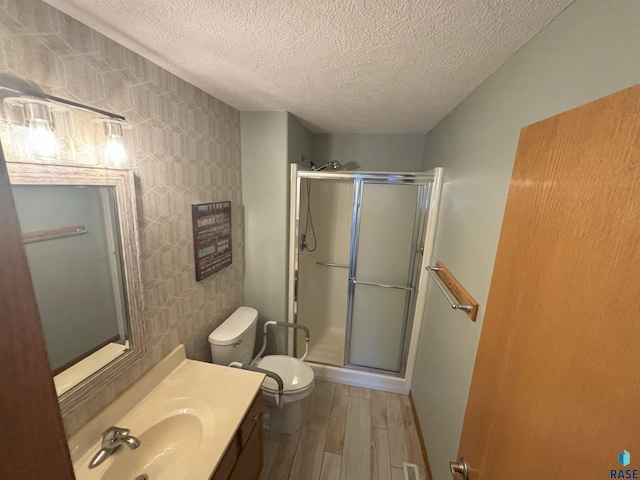 bathroom featuring vanity, a textured ceiling, hardwood / wood-style flooring, toilet, and a shower with shower door