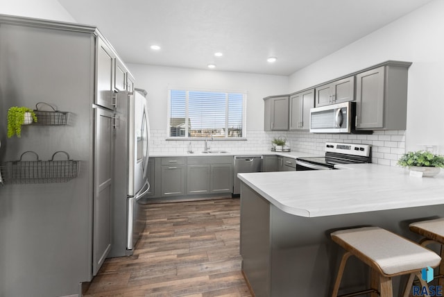 kitchen featuring sink, dark hardwood / wood-style floors, kitchen peninsula, a kitchen bar, and appliances with stainless steel finishes