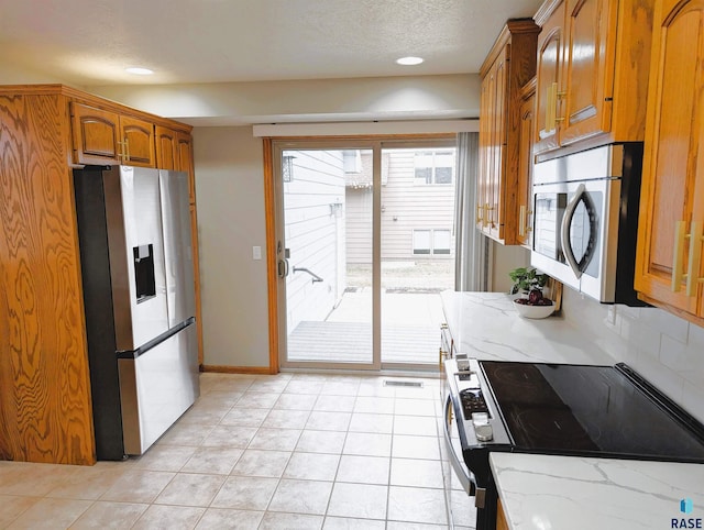 kitchen featuring appliances with stainless steel finishes, a textured ceiling, light tile patterned floors, and light stone counters