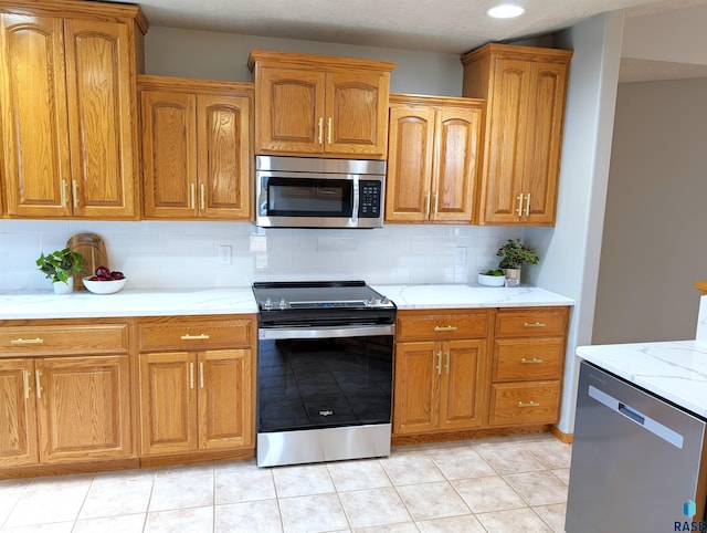 kitchen featuring decorative backsplash, appliances with stainless steel finishes, light stone counters, and light tile patterned flooring