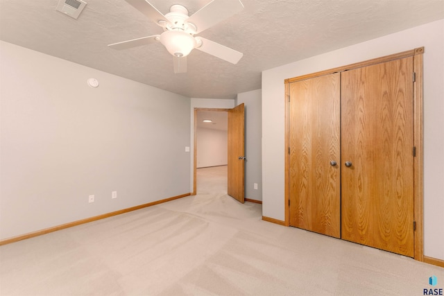 unfurnished bedroom with ceiling fan, a closet, light colored carpet, and a textured ceiling