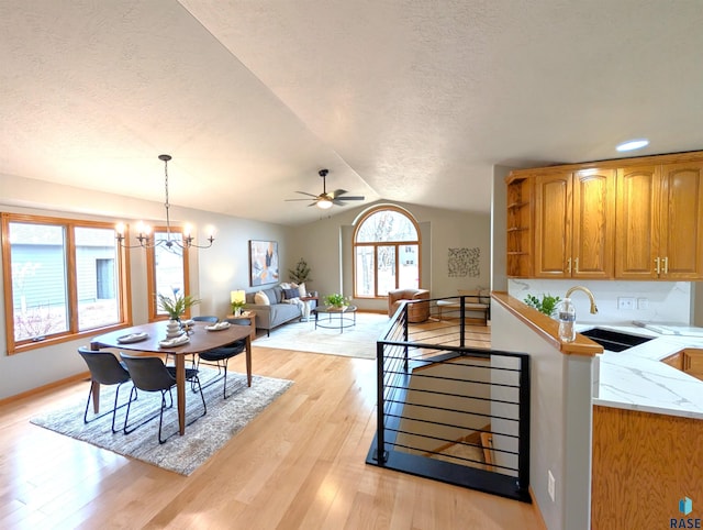 kitchen featuring sink, pendant lighting, vaulted ceiling, ceiling fan with notable chandelier, and light wood-type flooring