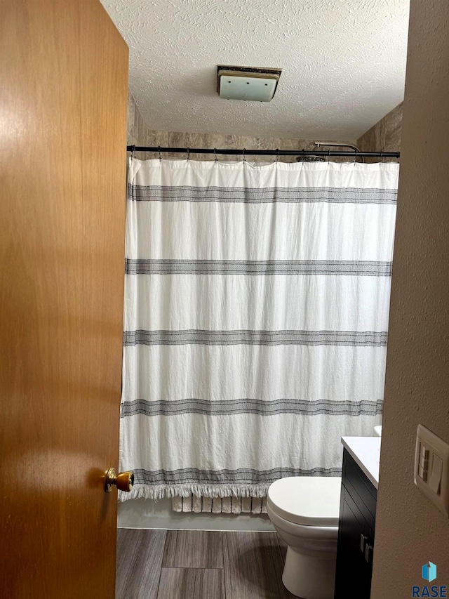 bathroom featuring a shower with curtain, vanity, toilet, and a textured ceiling