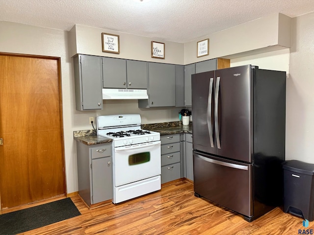 kitchen with a textured ceiling, gray cabinets, stainless steel refrigerator, and white gas range