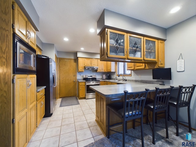 kitchen featuring a kitchen breakfast bar, appliances with stainless steel finishes, tasteful backsplash, light tile patterned flooring, and kitchen peninsula