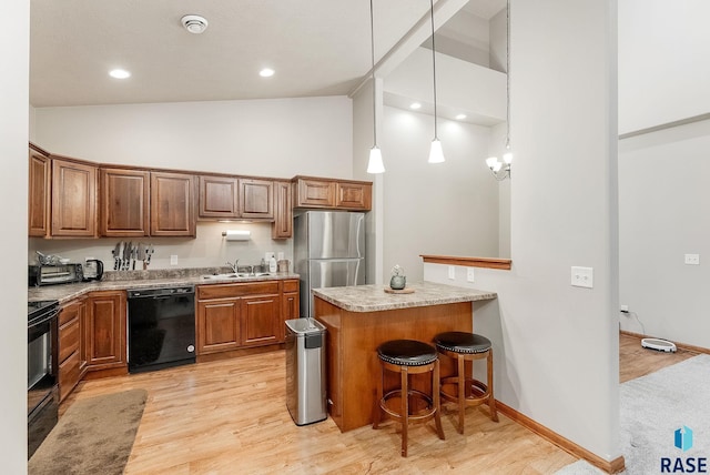 kitchen featuring sink, a kitchen breakfast bar, decorative light fixtures, black appliances, and light wood-type flooring