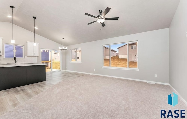 unfurnished living room with ceiling fan with notable chandelier, light hardwood / wood-style flooring, sink, and vaulted ceiling