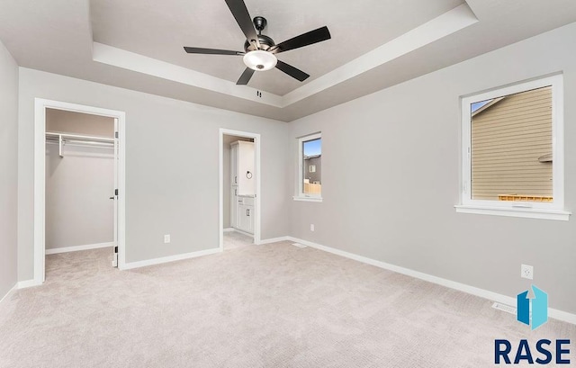 unfurnished bedroom with a walk in closet, a closet, a raised ceiling, and ceiling fan