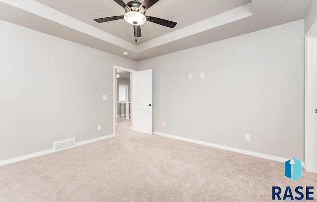 spare room with a tray ceiling, ceiling fan, and light carpet